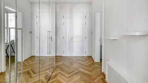 A hallway with white doors, a herringbone wood floor, and a glass partition.