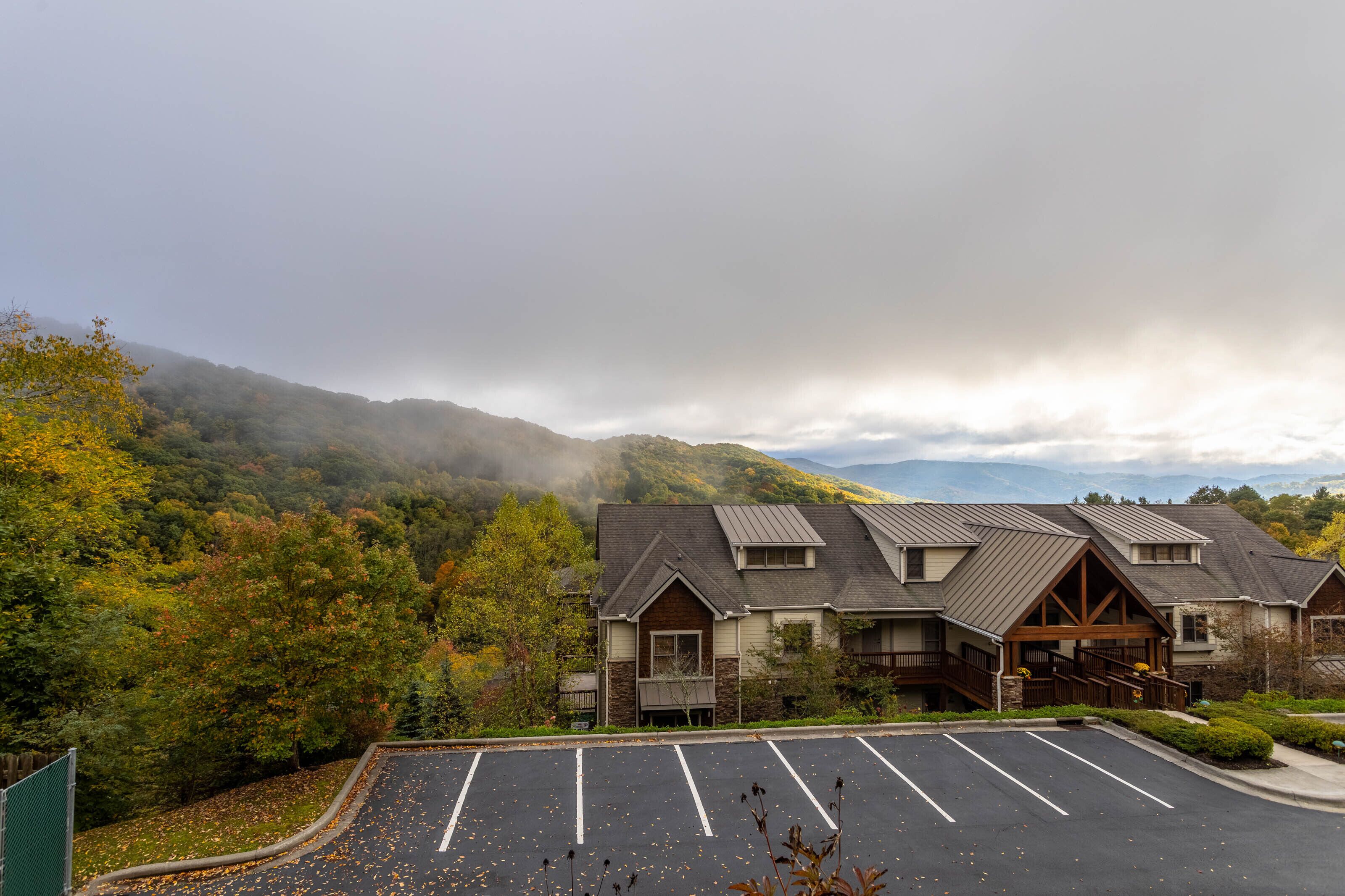 A lodge with a parking lot, surrounded by autumn foliage and mountains.