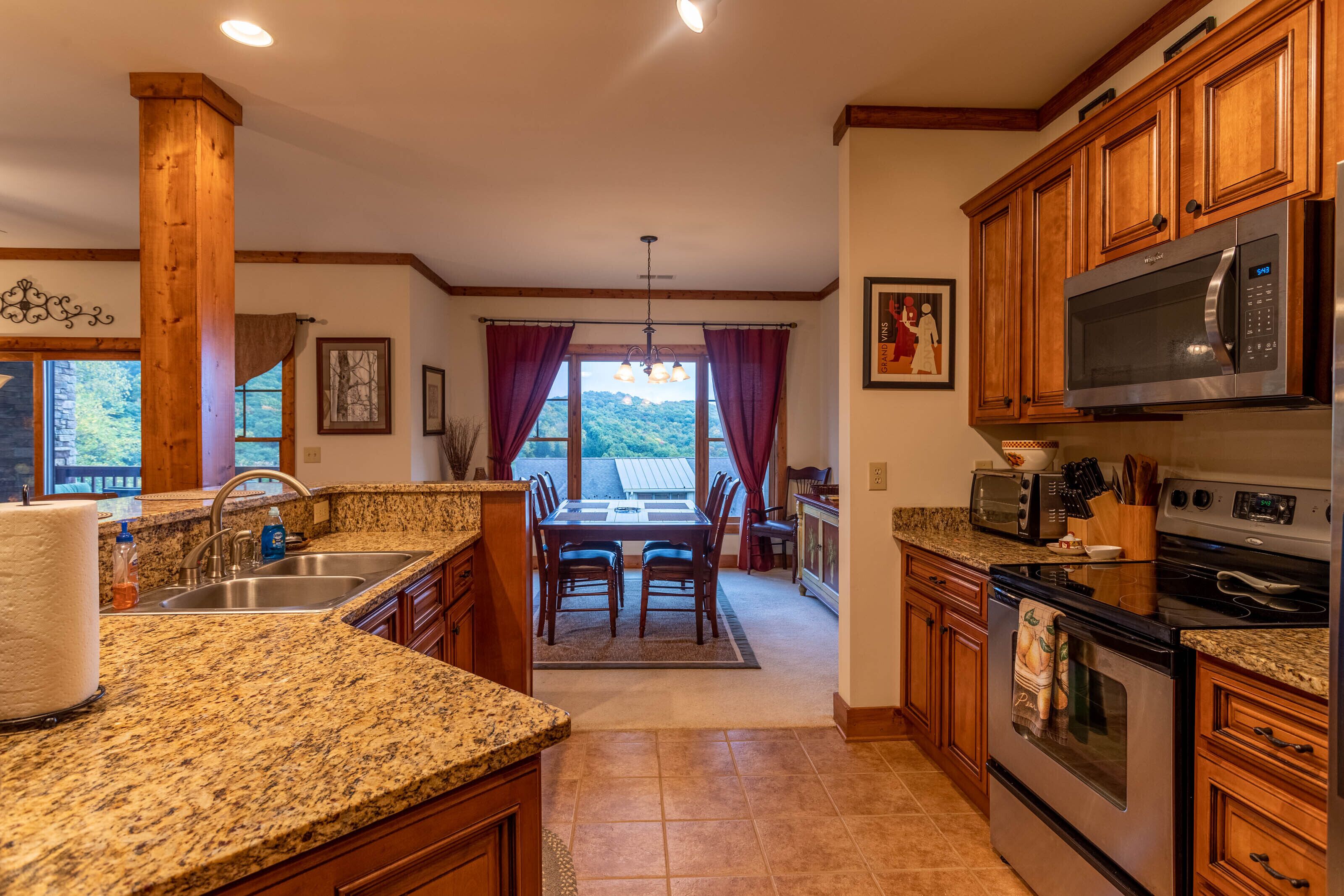 A kitchen with granite countertops, wooden cabinets, a stainless steel sink, a built-in microwave, and an oven.