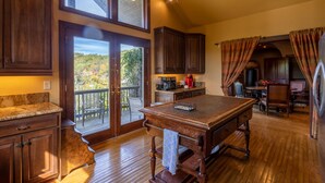 Une cuisine spacieuse avec des meubles en bois, une grande table en bois et une vue sur un balcon donnant sur un paysage extérieur.