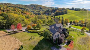 Une grande maison à deux étages, dotée d’un vaste jardin à l’avant, et entourée d’un paysage vallonné aux couleurs automnales.