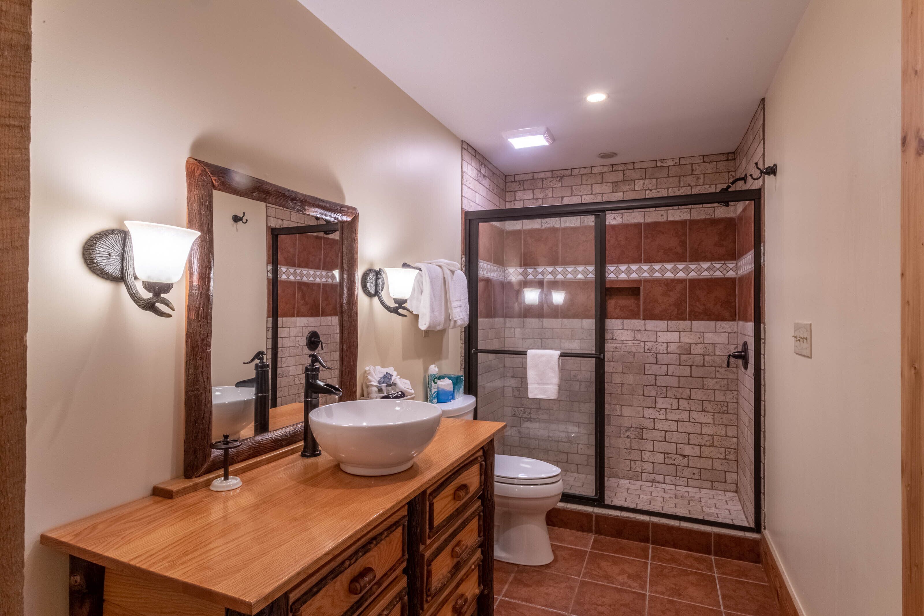 A bathroom with a wooden vanity, a large mirror, a white sink, a toilet, and a glass-enclosed shower area.