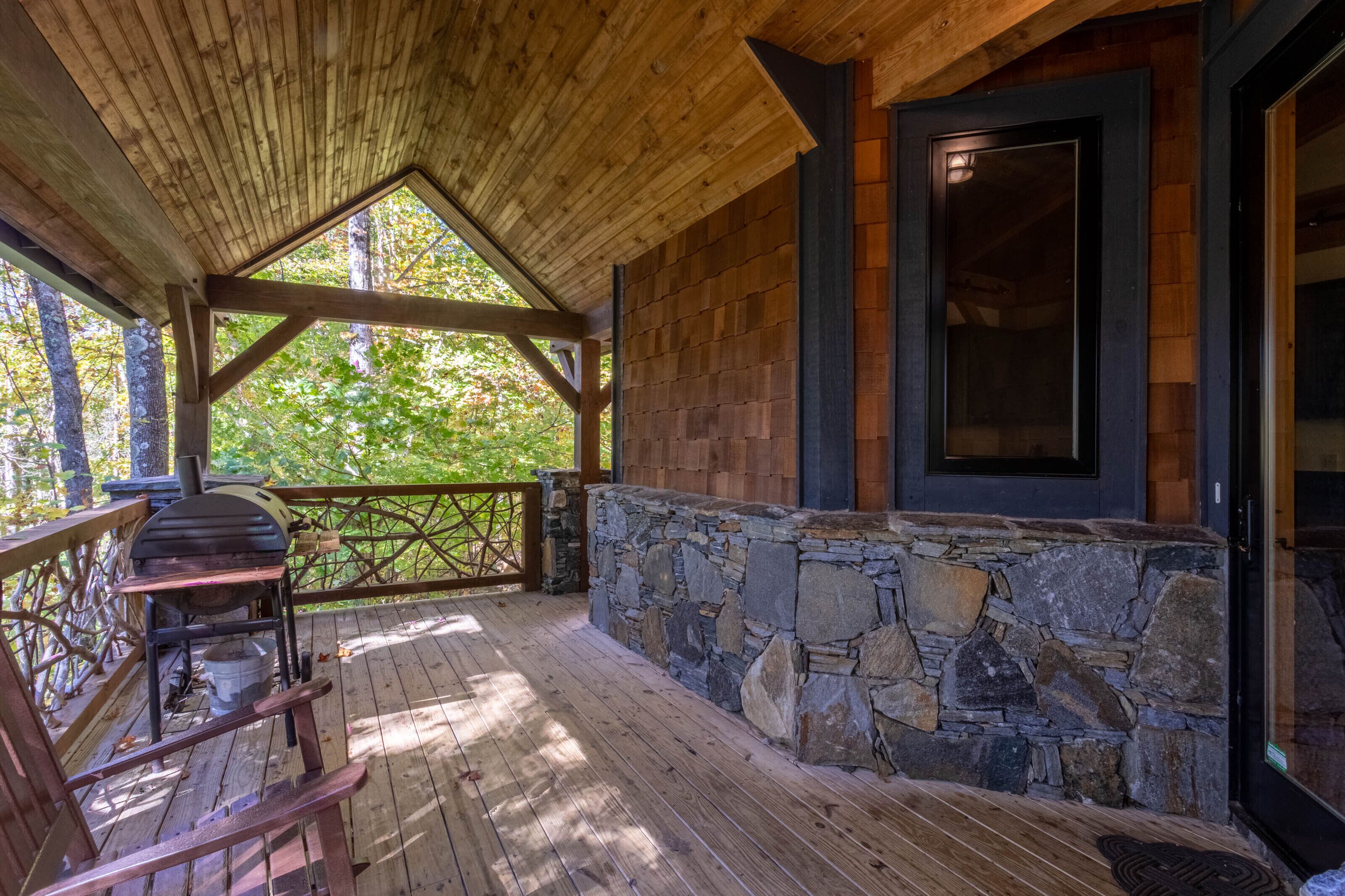 Une terrasse en bois couverte, avec un mur en pierre et un barbecue.