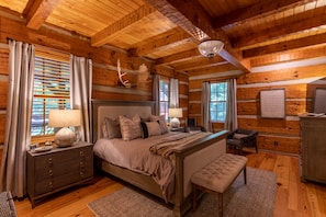 A log cabin bedroom with a large bed, a bench, a dresser, and a chandelier.