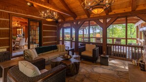 A log cabin interior with a wooden ceiling, chandeliers, a stone floor, and a view of the outdoors. - The Matney Ridge Estate- home with hot tub and firepit (Banner Elk)