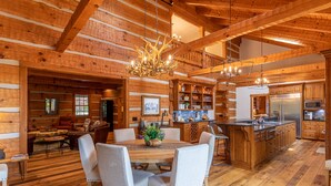 A spacious log cabin interior with a large dining area, wooden ceiling beams, and a central chandelier. - The Matney Ridge Estate- home with hot tub and firepit (Banner Elk)