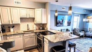 A modern kitchen with white cabinets, a granite countertop, a built-in oven, and a large island with stools.