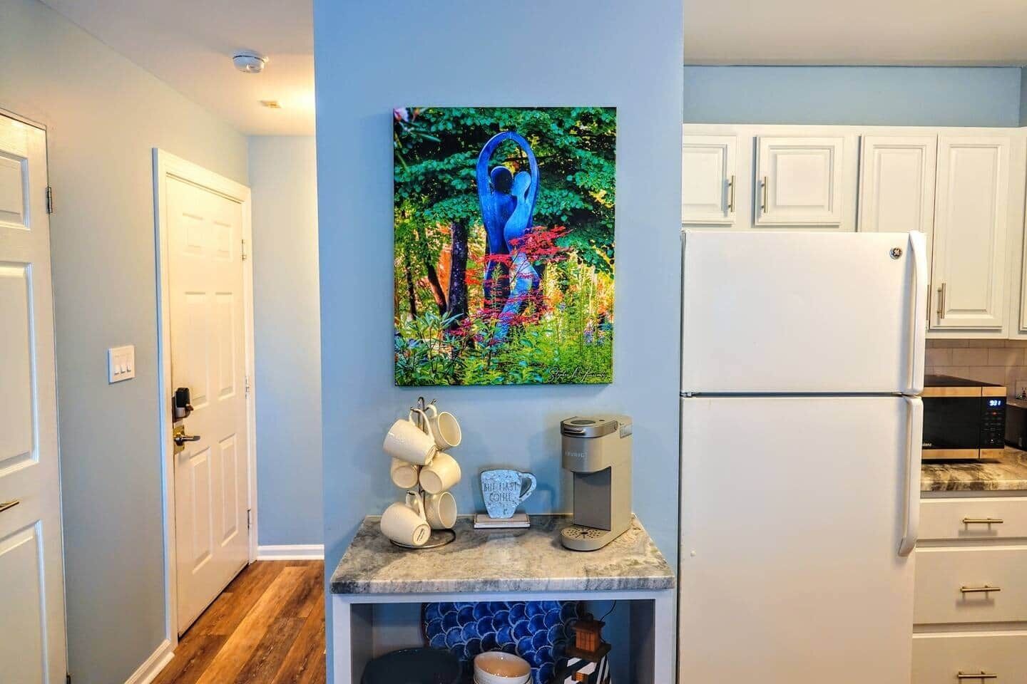 A kitchen with white cabinets, a coffee machine, and a colorful painting on the wall.