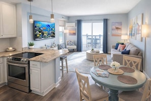 Een moderne keuken met een ingebouwde kookplaat, een eethoek met een ronde tafel en stoelen, en een woonkamer met een bank en een televisie.