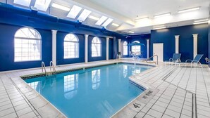 An indoor swimming pool with clear blue water, large arched windows, and a tiled floor.