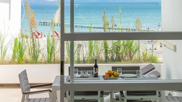 Un balcón con una mesa dispuesta para comer, con vista a una playa que tiene un muelle y gente.
