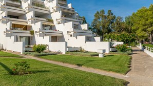 Un edificio moderno de varios pisos con balcones, un césped cuidado y un cielo despejado.
