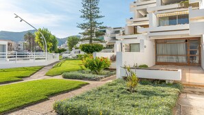 Un edificio residencial moderno con varios balcones, un jardín cuidado con diversas plantas y flores, y una vista despejada del entorno.