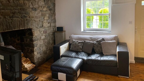 Ein gemütliches Wohnzimmer mit Kamin aus Stein, einer Ledersofa und einem großen Fenster mit Blick auf Grünflächen.