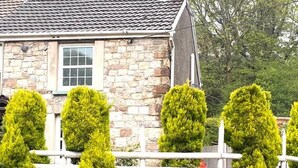 Ein Haus aus Stein mit einem Ziegeldach, einem Schornstein und einem weißen Zaun mit geschnittenen Büschen.