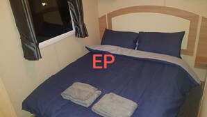 Ein Einzelbett mit blauer Bettdecke und Kissen, ein Fenster mit Vorhängen und ein Holz-Kopfteil.