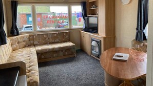 Ein kompaktes Wohnmobil-Interieur mit einer Sitzecke, einem kleinen Tisch, einem Fernseher und einer Wanduhr.