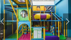 Un espace de jeux intérieur comprenant diverses structures d’escalade et un toboggan.