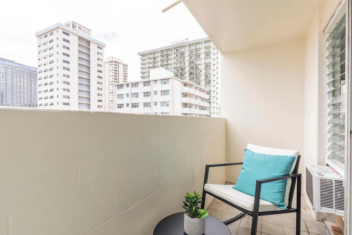 A balcony with a chair and a small plant, overlooking a cityscape with high-rise buildings.