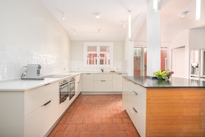 A modern kitchen with white cabinetry, a brick floor, and a window with shutters.