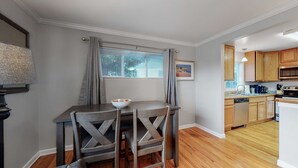 Una cocina compacta con armarios de madera, una mesa de comedor con dos sillas, una ventana con persianas y un pequeño rincón de comedor.