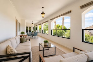 A spacious living area with a sofa, coffee table, and dining table. Large windows offer views of trees and a clear sky.