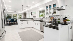 A modern kitchen with white cabinetry, a gas stove, and a dining area with a table and chairs. - The Gatsby I By Hotel Home Stays (Mesa)