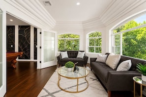 A spacious living room with a dark grey sofa, a round glass coffee table, and a pool table.