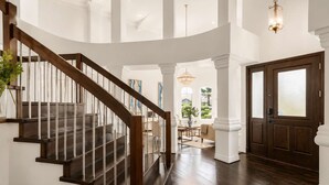 A grand staircase leading to a high-ceilinged room with a chandelier, a wooden door, and a view of the outdoors. - The Gatsby I By Hotel Home Stays (Mesa)