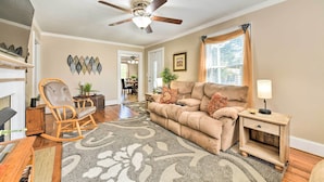A living room with a beige sofa, a rocking chair, a coffee table, a side table with a lamp, and a ceiling fan.