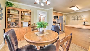 A dining area with a round wooden table, leather chairs, a ceiling fan, and a kitchen in the background.