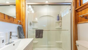 A modern bathroom with a glass-enclosed shower, a white sink, and wooden cabinetry. - Vacation UniquEly cottage #2 (Ely)