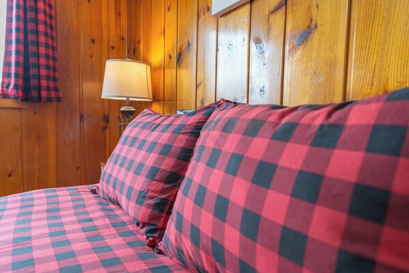 A bed with checkered bedding in a room with wooden walls and a lamp.