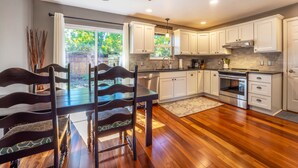 A modern kitchen with white cabinets, a built-in oven, and a dining area with a wooden table and chairs. - Devon Court - Adorable Remodeled, Quiet, Near Town, Fenced Yard, Pet Friendly (Hood River)