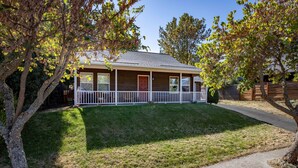 A two-story house with a front porch, a small front yard, and a wooden fence. - Devon Court - Adorable Remodeled, Quiet, Near Town, Fenced Yard, Pet Friendly (Hood River)