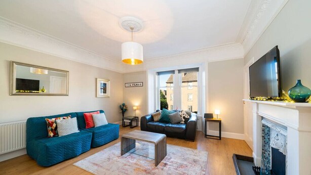 A living room with a blue sofa, a wooden coffee table, a fireplace, and a television. - Manor Place - Convenience and Style (Broughty Ferry, Dundee)