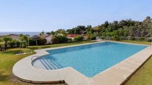 A rectangular swimming pool with a curved edge, surrounded by a grassy area and trees. - Nice Apartment with a Sunny Terrace, Pool & Sea View (Benalmádena)