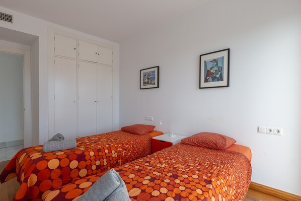 A room with two beds, a wardrobe, and two framed pictures on the wall.
