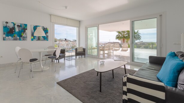 A modern living room with a dining area, large windows, and a view of the sea. - Nice Apartment with a Sunny Terrace, Pool & Sea View (Benalmádena)
