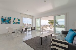 A modern living room with a dining area, large windows, and a view of the sea.