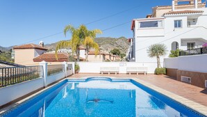 A swimming pool with a person swimming, surrounded by buildings and palm trees. - Homely apartment, 2 big terraces, stunning views and pool (Nerja)