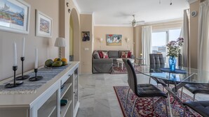 A modern living room with a glass dining table, a sofa, and a ceiling fan. - Homely apartment, 2 big terraces, stunning views and pool (Nerja)