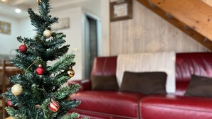 Un pequeño árbol de Navidad con adornos en una sala de estar con un sofá de cuero rojo y vigas de madera.