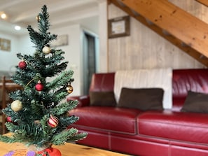 A small Christmas tree with ornaments in a living room with a red leather couch and wooden beams.
