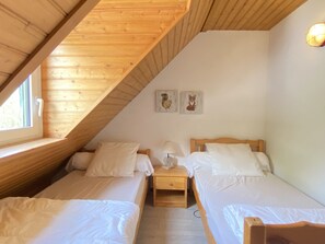 A cozy attic bedroom with two single beds, a nightstand, and a window.