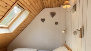 Un dormitorio con techo inclinado, tragaluces, cama con ropa de cama blanca y apliques decorativos en la pared.