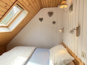 A bedroom with a sloped ceiling, a skylight, a bed with white bedding, and decorative wall sconces.