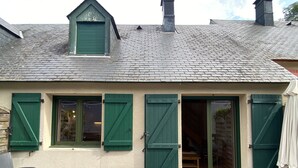 A house with a sloped roof, green shutters, and a wooden deck with chairs. - Le 103. Chalet 3 chambres. Terrasse. Parking. wifi (Cauterets)