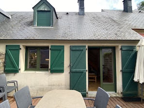 A house with a sloped roof, green shutters, and a wooden deck with chairs.