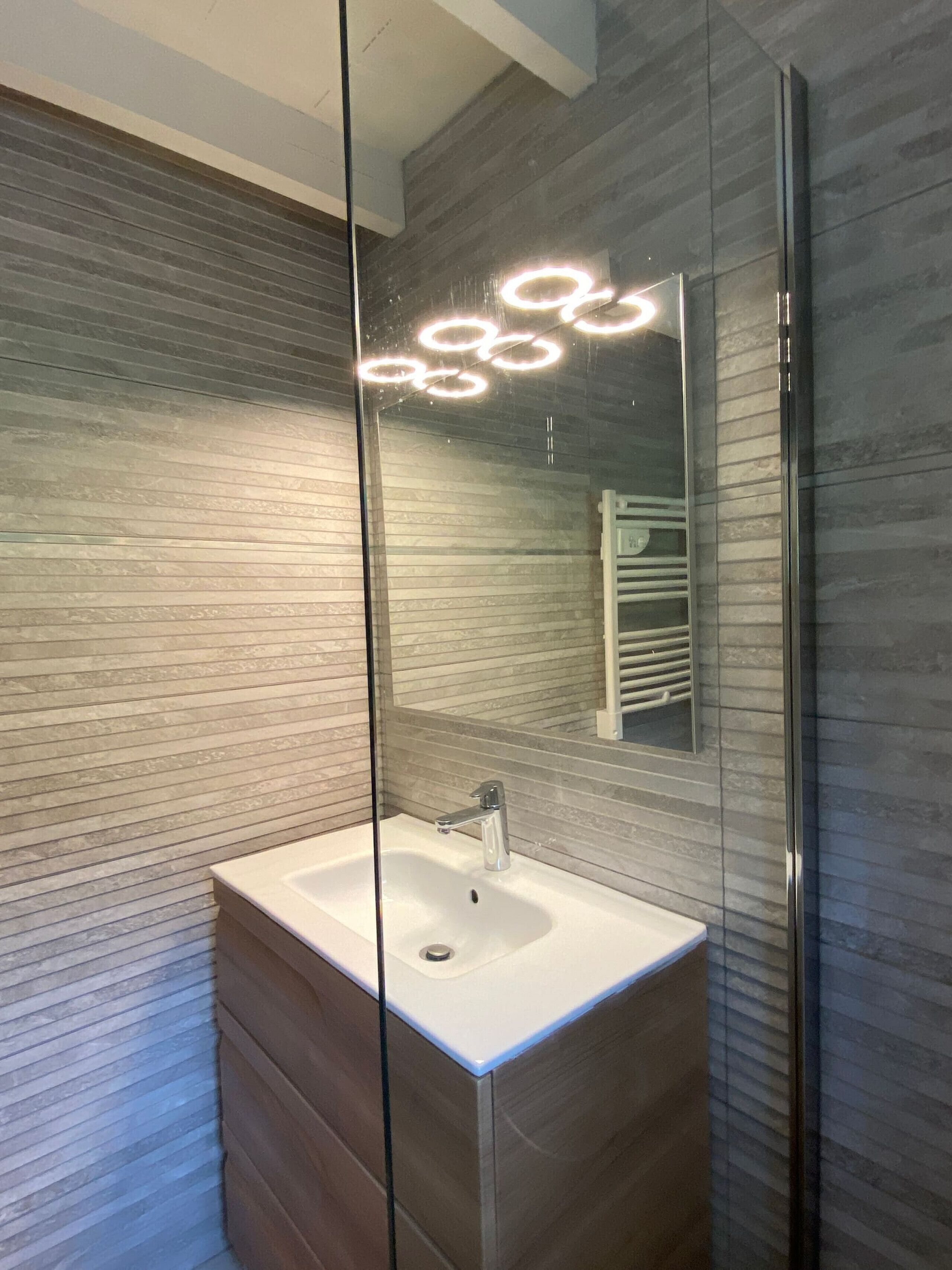 A modern bathroom with a glass partition, a white sink, and a mirror reflecting a towel rack.